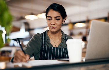 Image showing Small business owner working on a budget in her coffee shop and writing a list of stock to order. Serious female entrepreneur developing a growth strategy for her cafe startup
