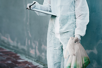 Image showing Forensic investigator collecting evidence on a murder scene on a street holding a plastic bag and wearing a hazmat suit. Crime researcher doing a scientific criminal investigation outdoors in a city