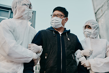 Image showing Asian man breaking covid regulation getting taken away or arrested by healthcare workers wearing hazmat protective suits. Male removed for not following the rules or restrictions of the pandemic.