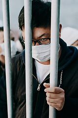 Image showing Lockdown, isolation and covid travel ban with a man in a mask behind bars during an international pandemic. Corona virus restrictions, feeling like a prisoner or captive during a global shutdown