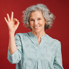 Image showing Good, perfect and okay with a senior woman hand gesture or sign in support or positive backing in studio against a red background. Portrait of a mature female looking motivated, happy and smiling