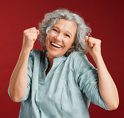 Image showing Celebrating, cheering and winning with a happy, smiling and excited senior female posing in studio against a red background. Portrait of a cheerful, wow and positive mature female with a fist gesture