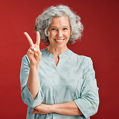 Image showing .. Senior woman express peace sign, v gesture and emoji with fingers on red studio background. Portrait of carefree, cool and smiling lady in positive, playful and fun mood showing victory with hand.