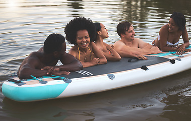 Image showing Friends, swimming and summer break with paddle board in a lake, ocean or sea over holiday, vacation or weekend. Diverse group of men and women bonding together, having fun and being playful or social