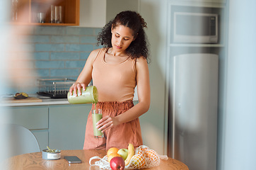 Image showing Healthy, nutrition and wellness smoothie made by young woman for her fresh, green detox or vegan diet at home in her kitchen. Vegetarian female pouring and drinking her organic homemade fruit juice