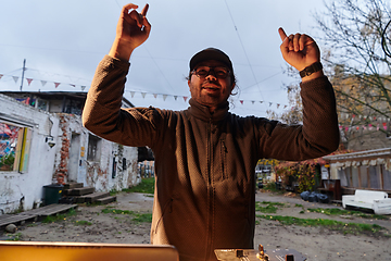 Image showing A young man is entertaining a group of friends in the backyard of his house, becoming their DJ and playing music in a casual outdoor gathering