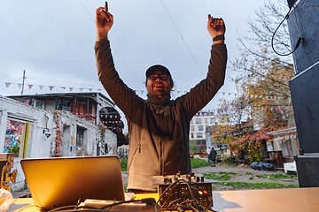 Image showing A young man is entertaining a group of friends in the backyard of his house, becoming their DJ and playing music in a casual outdoor gathering