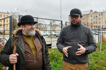 Image showing In the picturesque garden of Riga, Latvia, a man engages in a heartfelt conversation with his older friend, enjoying the serene urban oasis amidst the bustling cityscape