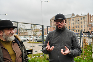 Image showing In the picturesque garden of Riga, Latvia, a man engages in a heartfelt conversation with his older friend, enjoying the serene urban oasis amidst the bustling cityscape