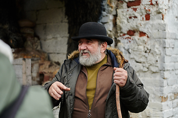 Image showing An elderly man with a beard and a worn hat passionately imparts traditional values and cultural wisdom to others, embodying the essence of heritage preservation and storytelling.