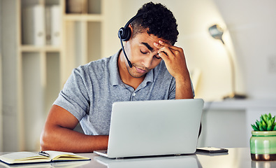 Image showing Stressed, tired and frustrated call center agent feeling sick or ill in the office while working on his laptop. A worried and unhappy young telemarketing employee suffering from a headache and pain