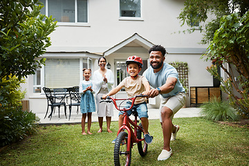 Image showing Boy on bicycle learning with proud dad and happy family in their home garden outdoors. Smiling father teaching fun skill, helping and supporting his excited young son to ride, cycle and pedal a bike