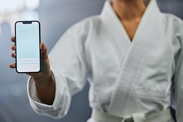 Image showing . Blank phone screen and copyspace with a karate student holding the mobile display indoors. Sport person showing a copy space announcing a sale, marketing or social media advertising content.
