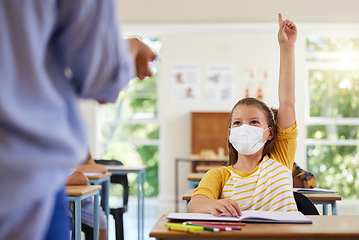 Image showing Smart student with covid face mask asking teacher question about corona virus pandemic in a classroom or elementary school. Little girl child raising hand to answer healthcare related topic in class