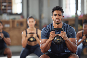 Image showing Personal trainer squatting with a team of athletes in a workout session at a fitness club. Portrait of a fit, active and serious young male coach using a kettlebell and training a group of people