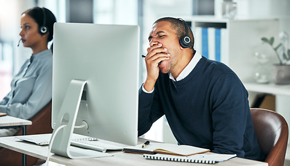 Image showing Tired call center agent yawning while sitting at his desk working on a computer in the office. Exhausted, bored and rude man in financial customer service feeling fatigue after a long day at work.