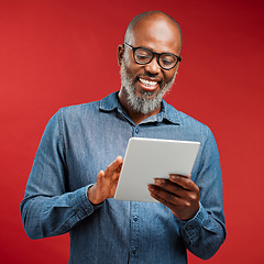Image showing Smiling man browsing on a tablet online, networking on the internet and scrolling on an app while standing against a red studio background. Happy, mature and African male reading an email and typing