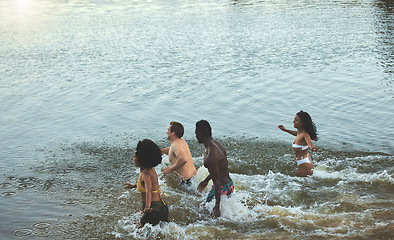Image showing Swimming, fun and freedom in the sea with a group of young friends taking a swim in the ocean by the beach while on holiday or vacation. Diverse people playing, bonding and feeling carefree together