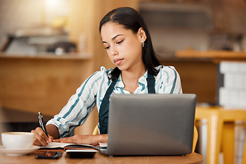 Image showing Cafe owner, coffee shop manager or small business entrepreneur writing notes and working on a laptop in her startup. Young female looking serious while managing finance and capital of her bistro