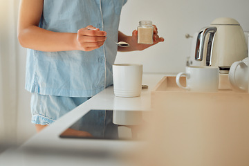 Image showing Casual woman adding sugar while preparing a cup of coffee, tea or hot chocolate in the kitchen during the morning. Female hands holding teaspoon for a fresh beverage in a mug for breakfast at home