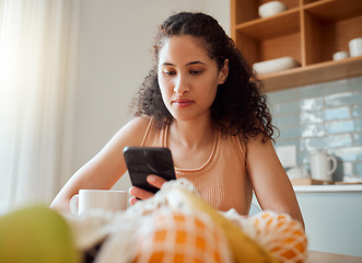 Image showing Healthy, wellness lifestyle woman sitting at home kitchen table scrolling on social media on her phone during breakfast. Young female enjoying her cup of coffee while texting in the morning