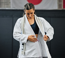 Image showing . Female professional karate student dressing, wearing and preparing for practice, fight or training match in dojo. Woman mix martial art athlete tying uniform before competition or exercise workout.