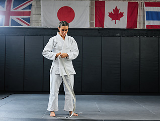 Image showing Professional karate student dressing and prepare for practice in a dojo or club. Female mix martial art athlete tying belt in training for a fight, competition or exercise workout in a sport studio