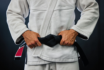 Image showing . Professional karate master holding a black belt against a dark background in a dojo. Trainer, coach or leader prepared and motivated for training, fitness exercise and fight practice in a dojo.