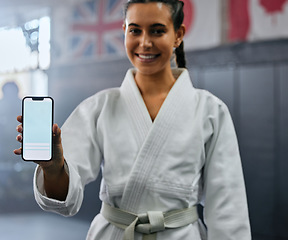 Image showing Portrait of a female karate student holding tech with social media, looking active and fit at class. Blank screen on phone, showing a fitness app and training website while standing at a sports gym.