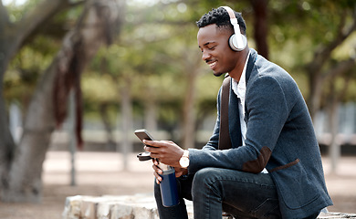 Image showing Businessman browsing social media on his phone and enjoying his music playlist app in headphones outdoors. Young, happy and casual african male relaxing in a nature park outside during a break