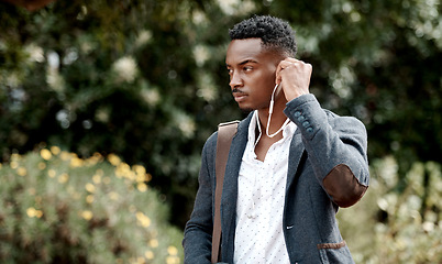 Image showing A stylish, trendy and serious young man going to work while listening to music using earphones. A young African American male entrepreneur walking outdoors with nice style or fashion