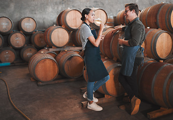 Image showing Wine distillery owners tasting the produce in the cellar standing by the barrels. Oenologists or sommeliers drinking a glass of chardonnay or sauvignon blanc inside a winery testing the quality