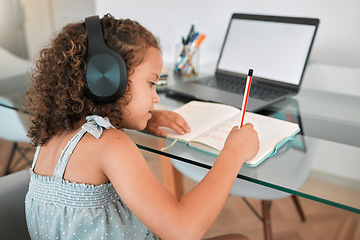 Image showing Homeschooling by a smart and clever little girl attending online or virtual class using a laptop and headphones. A young child writing and working or doing homework at home listening to music