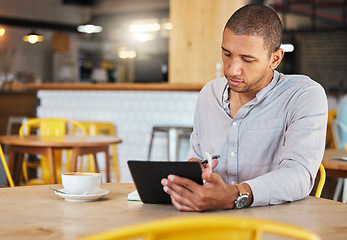 Image showing Serious freelance business man working in a coffee shop doing remote work for his startup. Young male entrepreneur using a tablet planning growth strategy in a cafe and writing notes