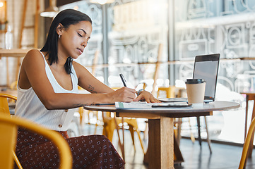 Image showing Student writing, taking notes or doing a project assignment in cafe or restaurant using laptop and notebook. Young woman taking an online education class or doing study work, learning in coffee shop.