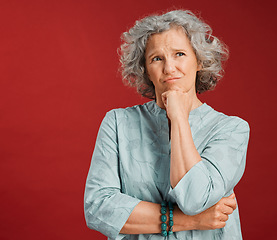 Image showing Thinking, confused and wondering woman looking puzzled, unsure and uncertain about choice, decision and idea in mind against studio red background. Thoughtful senior woman with goofy frown expression