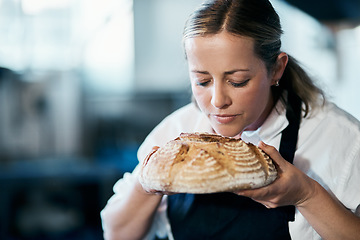 Image showing Baker, pastry chef and cafe owner smelling a loaf of fresh baked bread in the kitchen of her coffee shop. Closeup of a female cook enjoying the aroma of a freshly made dough treat or consumables