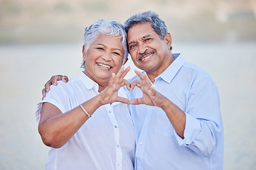 Image showing A happy senior couple with a heart sign with their fingers and enjoying fresh nature air on vacation at beach while bonding. Portrait of retired couple hugging at beach with smile and love together