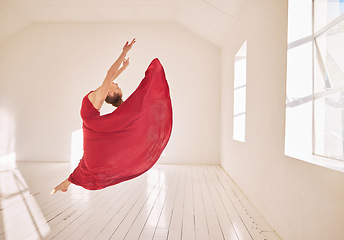 Image showing Woman, ballet and dance of a girl student dancing in a red dress in a studio mockup with white walls and sunlight. Young professional female ballerina, art or dancer jumping in the air in a class.