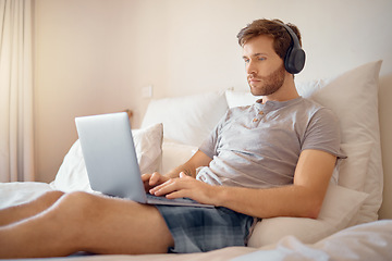 Image showing Man working or typing on laptop and listening to music with headphone in bed at home. Remote worker streaming podcast online while reading and send work email on wireless tach in the bedroom alone
