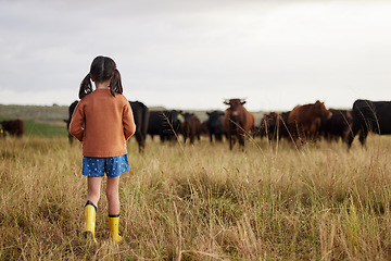 Image showing Little girl learning agriculture on a sustainability farm with cattle and exploring nature outdoors. Back view of a carefree child or kid watching cows or farmland animals enjoying the countryside