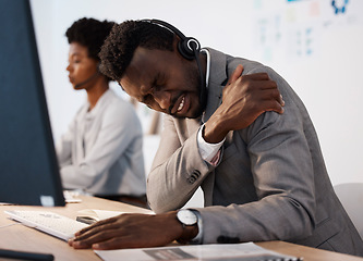 Image showing Pain, injury and hurt call center agent holding his shoulder in agony while working in the office. Young African American male customer service consultant suffering from a painful arm