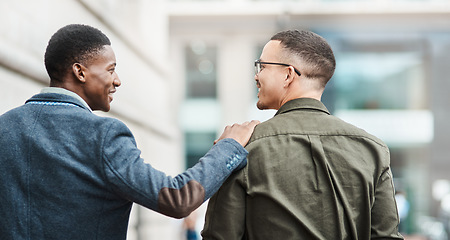 Image showing Two young businessmen smiling, talking and walking through the city together, excited for their new project. Happy multiracial coworkers strolling with his hand on his friends shoulder while laughing