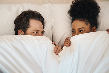 Image showing Interracial, happy and relaxed couple lying in bed, bonding and looking shy while hiding after waking up together in the morning. Loving, carefree and romantic boyfriend and girlfriend being intimate