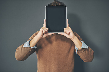 Image showing Young man holding a blank tablet up to his face, in casual wear against a gray background with copy space. Alone male standing with a blank screen pressed against his head. Adult posing with a device