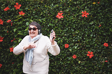 Image showing Funny old woman dancing listening to music on smartphone wearing earphones smiling enjoying fun celebrating retirement in garden with flower wall