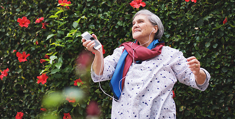 Image showing Funny old woman dancing listening to music on smartphone wearing earphones smiling enjoying fun celebrating retirement in garden with flower wall