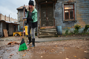 Image showing A woman diligently maintains the garden by collecting old, dry leaves, creating a picturesque scene of outdoor care and seasonal tidiness