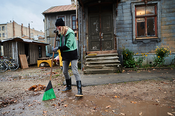 Image showing A woman diligently maintains the garden by collecting old, dry leaves, creating a picturesque scene of outdoor care and seasonal tidiness