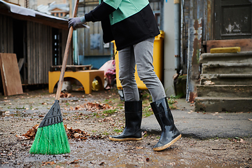 Image showing A woman diligently maintains the garden by collecting old, dry leaves, creating a picturesque scene of outdoor care and seasonal tidiness